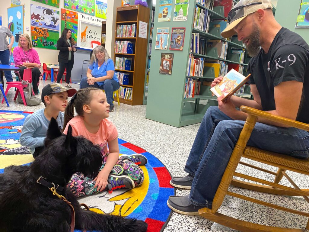 man sitting in chair reading book to kids